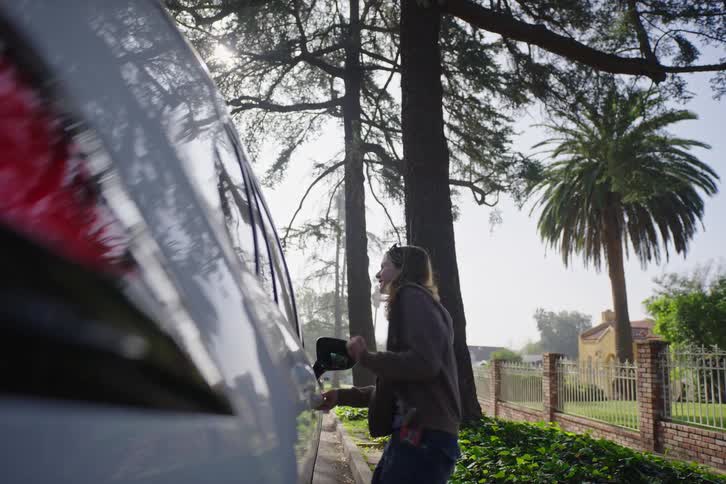 A happy young woman dances as she gets into a car on a sunny suburban street