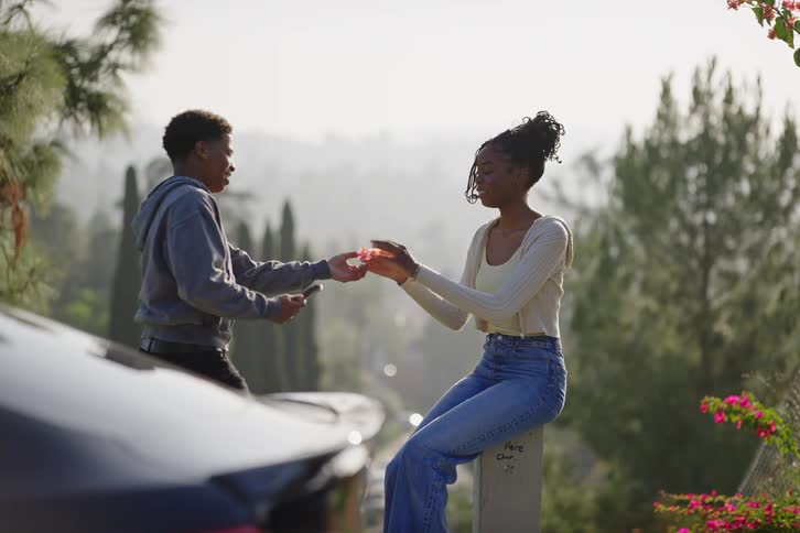 A young man takes photos of his smiling girlfriend with his phone after giving her a flower at a scenic overlook