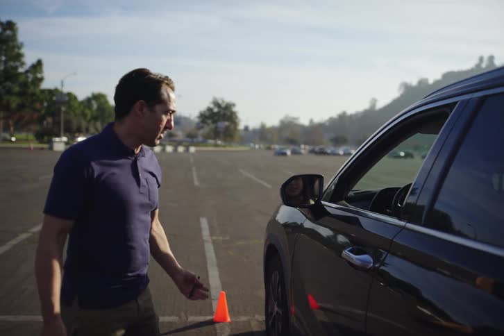 Slow motion shot of a driving instructor walking and giving directions to a student during a driving test in a parking lot