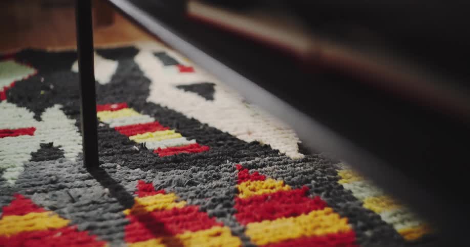 Flickering light casts moving shadows on a colorful patterned rug under a piece of furniture