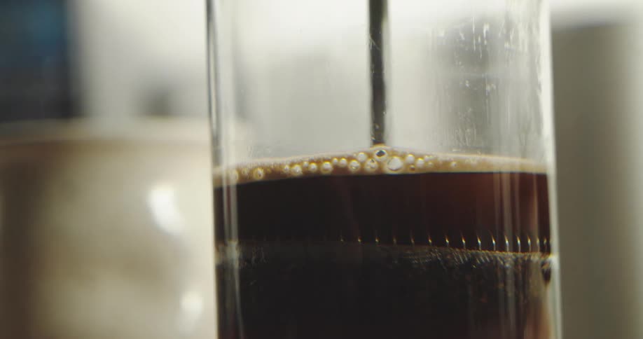 Macro shot of fresh coffee brewing in a French press as the filter is pushed down