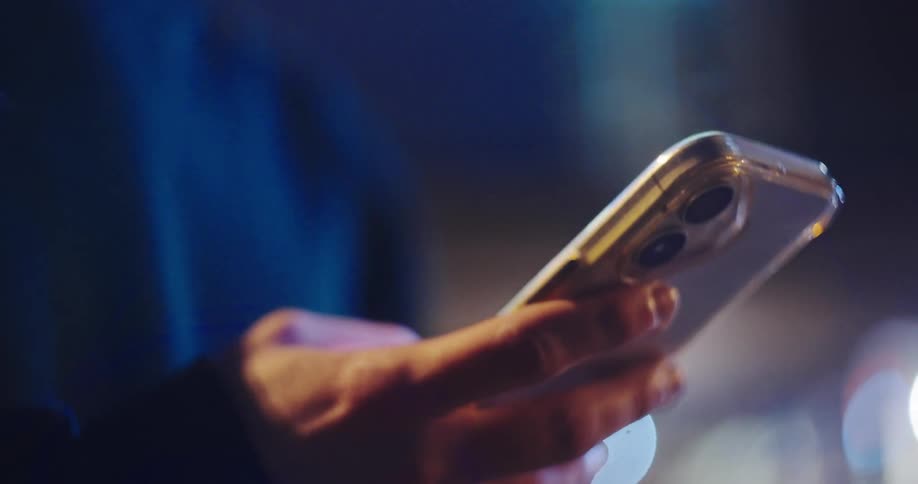 Close-up of a hand using a smartphone at night with blurry city lights in the background