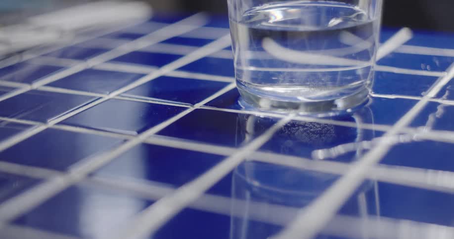 A close-up of an effervescent tablet dissolving and fizzing in a glass of water set on a blue tiled surface