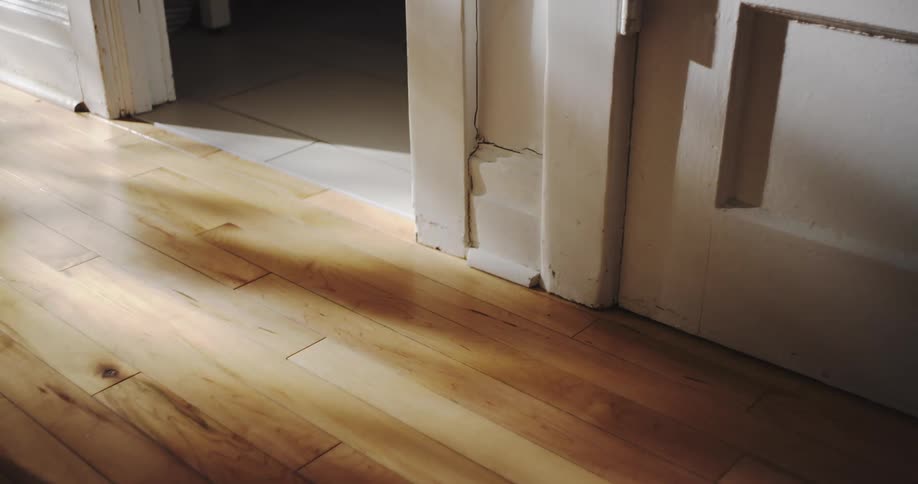 A time-lapse shows shadows from a window moving across a sunlit hardwood floor next to a white doorway