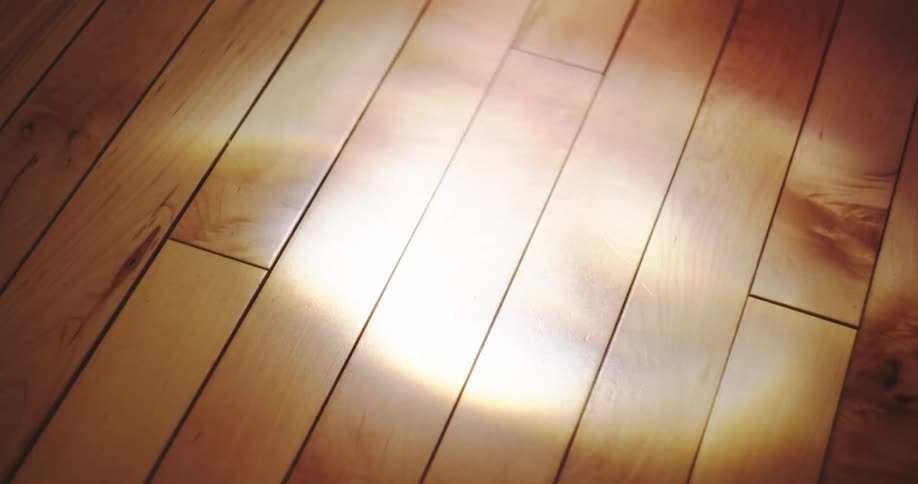 Close up of a warm, ethereal light reflection moving slowly across a polished hardwood floor