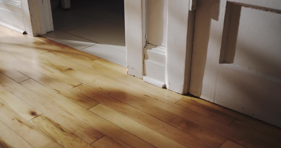 Red flashing emergency lights reflect on a hardwood floor and door frame, creating a suspenseful atmosphere