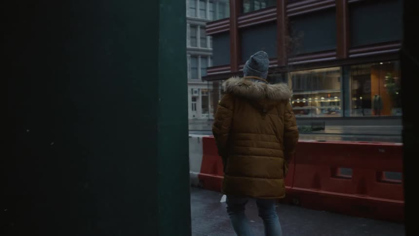 A man in a heavy coat walks on a city sidewalk