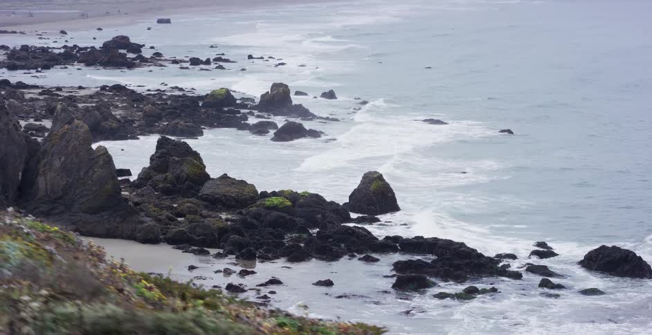 A slow-motion tracking shot along a rugged and rocky coastline on a moody, overcast day