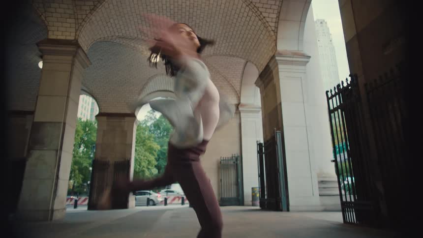 A graceful young Asian woman performs an expressive contemporary dance in slow motion under an arched city building