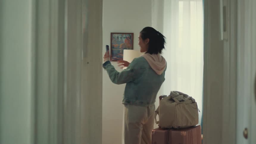 An excited young Asian woman arrives at her vacation rental and immediately takes out her smartphone to film a tour for her friends