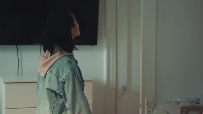 A happy young Asian woman texts on her phone and looks around her bright apartment before smiling and walking away