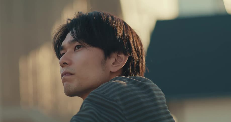 Close up of a thoughtful young Asian man looking into the distance with a serious expression during golden hour