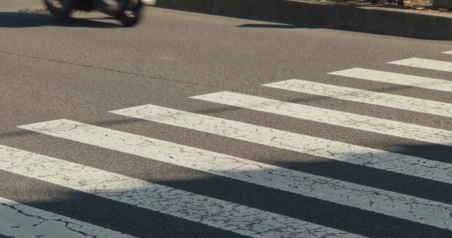 A close-up view of traffic driving over a crosswalk on a city street in the sun