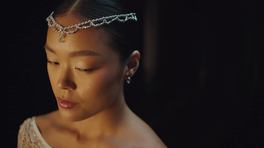 A cinematic close-up of a beautiful young Asian woman in a jeweled headpiece with a single tear on her cheek