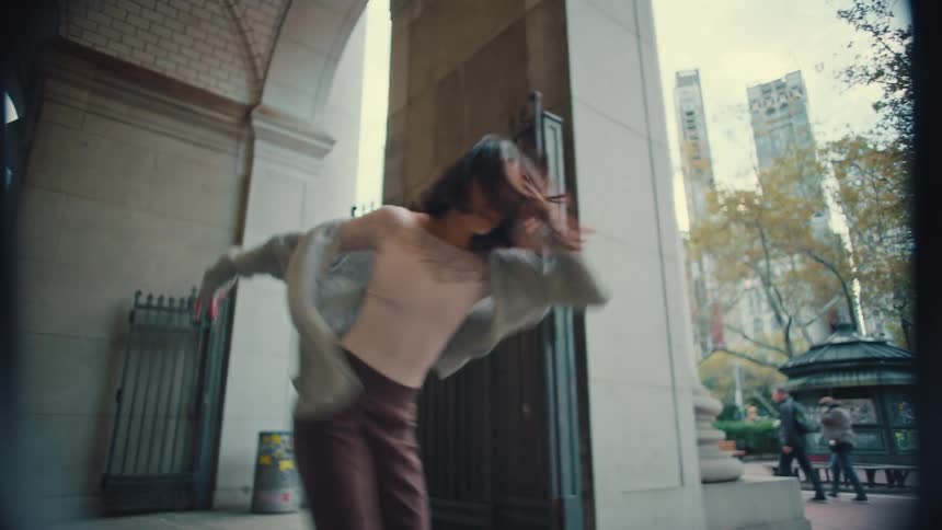 A barefoot woman performs a graceful and expressive contemporary dance in slow motion under a grand city archway