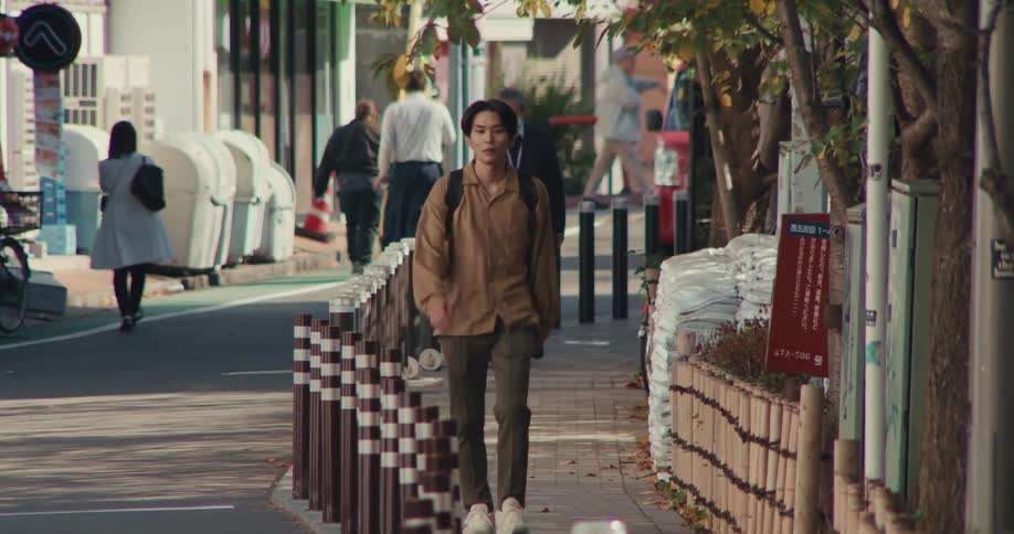 Slow motion shot of a young Japanese man with a backpack walking down a sidewalk in the city