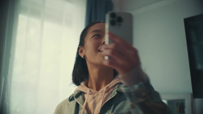 A joyful Asian woman having an animated video conversation on her mobile phone in her bedroom