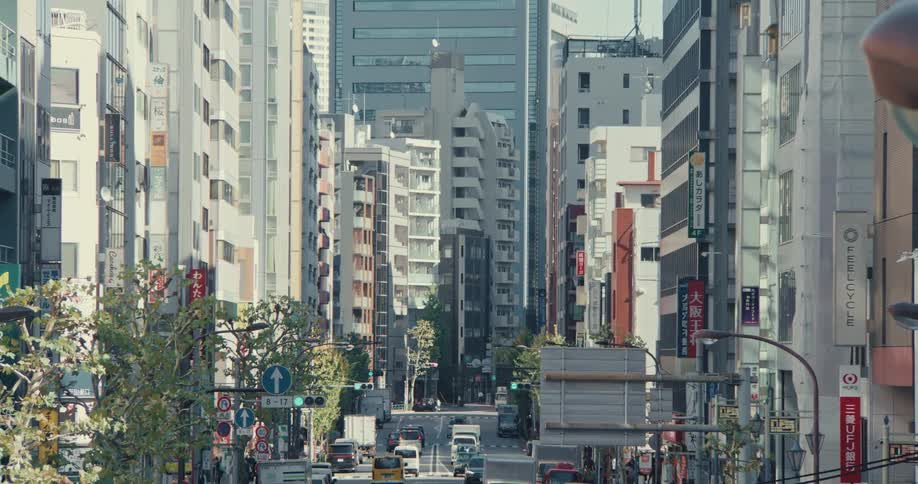 A long shot down a busy urban street canyon in a modern Japanese city during the day