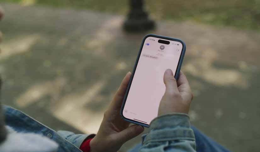 A person reads a sad text message saying 'I'm sorry Benedict!' on their smartphone while sitting on a park bench