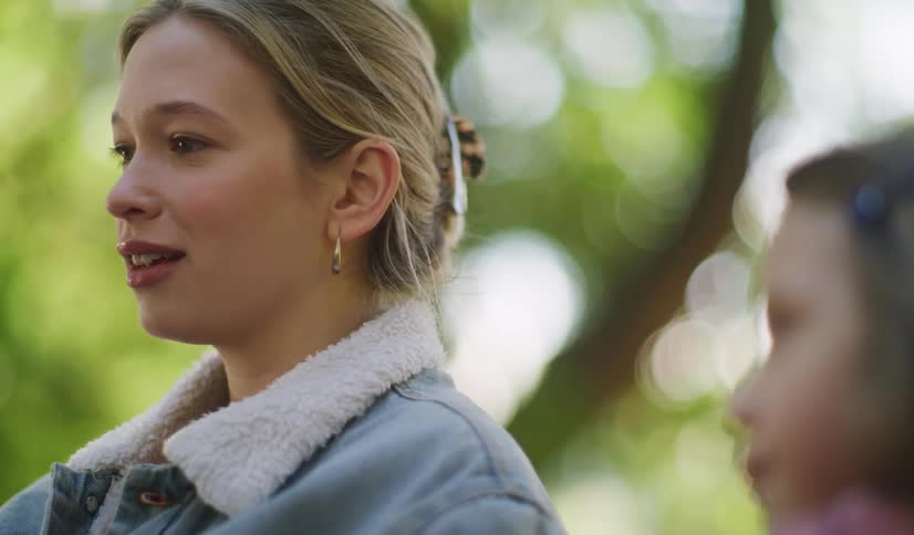 A blonde woman in a denim jacket shares a tender moment talking with a young girl outdoors