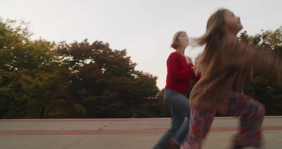 A joyful mother and daughter run and leap through a city park in a playful slow-motion chase