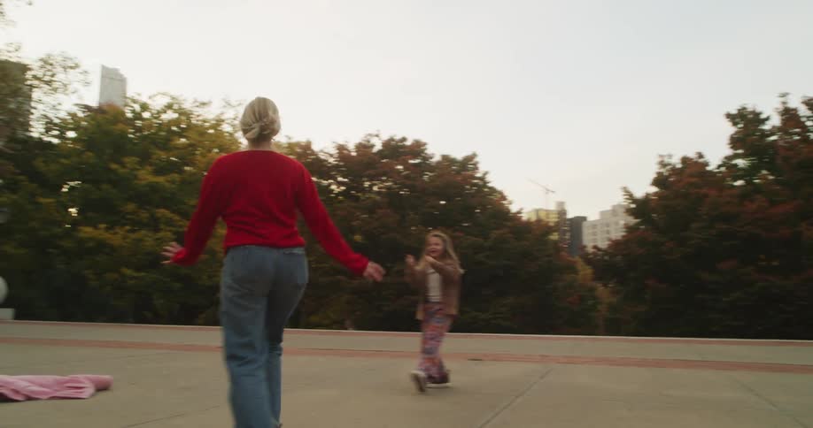 A mother and her young daughter take turns doing cartwheels in a city park, enjoying a playful autumn day together in slow motion