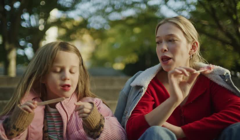 A mother and her young daughter sit on park steps together, enjoying a sweet popsicle treat on a cool afternoon
