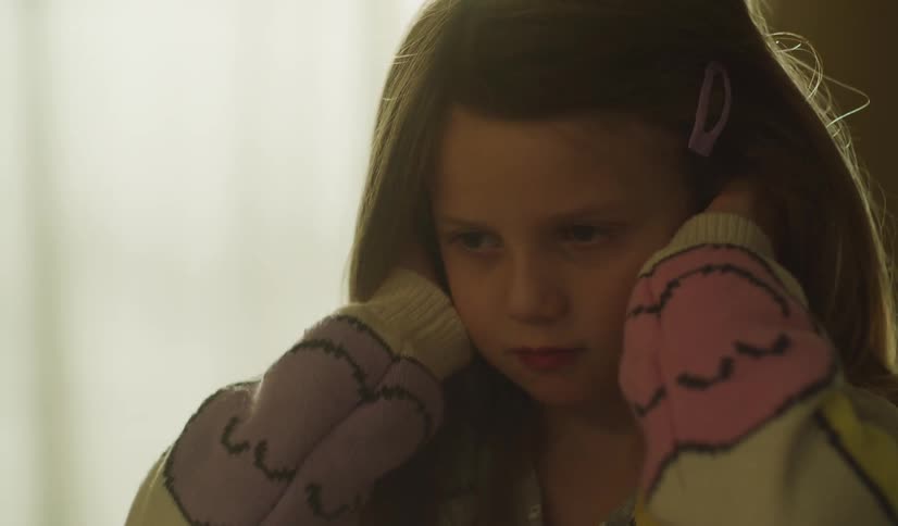 A troubled young girl covers her ears with her hands in slow motion to block out noise