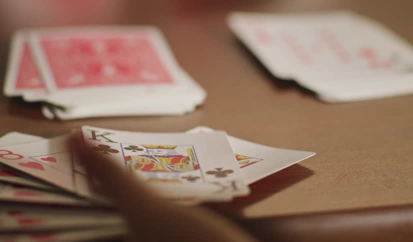 A person's hand lays down a fan of playing cards on a wooden table in slow motion