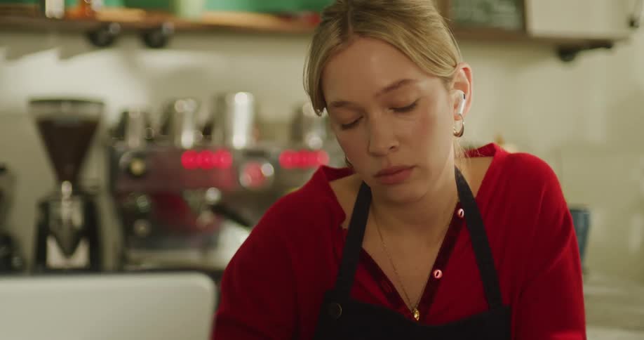 A young female barista wearing earbuds idly shuffles a deck of cards at the counter of a coffee shop during a slow moment