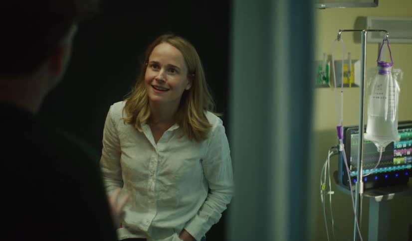 A worried mother has an intense conversation with a doctor while her teenage son sits silently in his hospital bed nearby