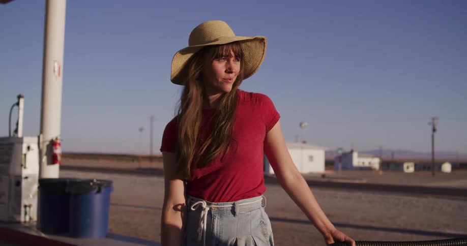 A slow-motion shot captures a woman at a remote desert gas station, which pans out to reveal the iconic Roy's Motel Cafe sign on a lonely highway