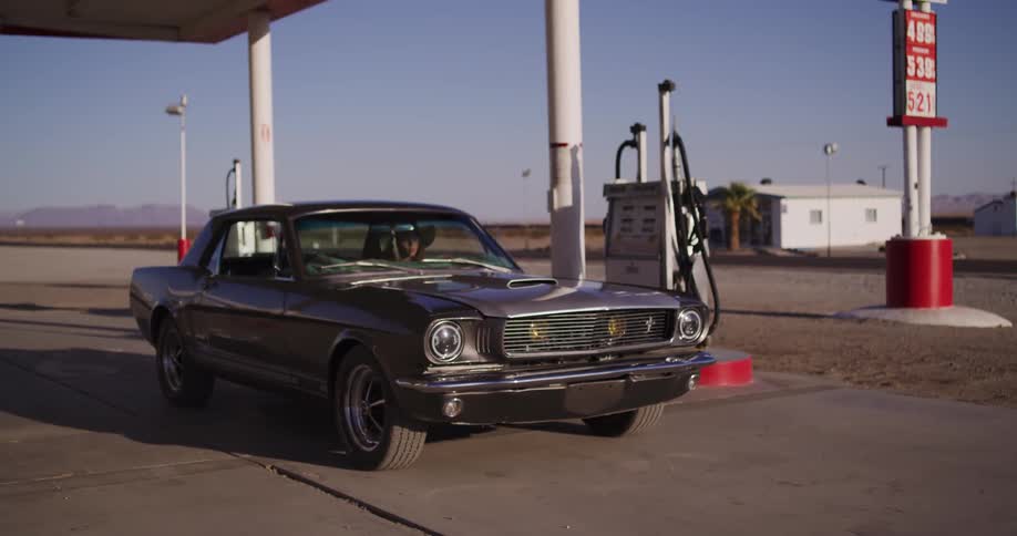 A woman in a vintage Ford Mustang pulls into a classic desert gas station on Route 66 to refuel her car