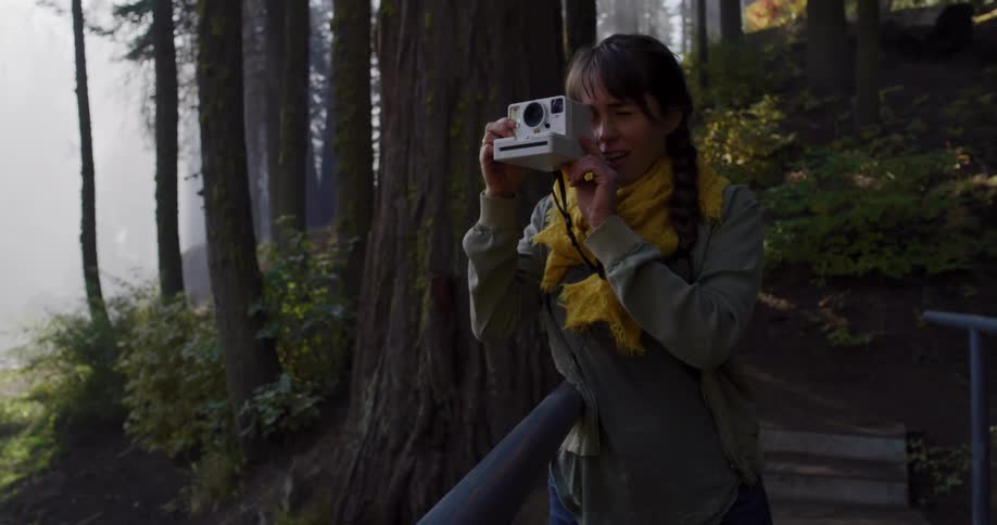 A happy young woman with an instant camera captures a memory while exploring a misty redwood forest