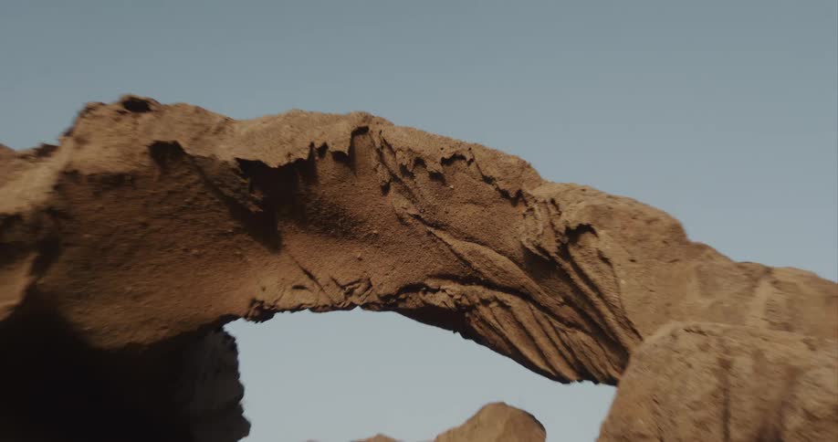 A camera slowly pushes in on the detailed, sandy texture of a natural rock arch against a clear sky