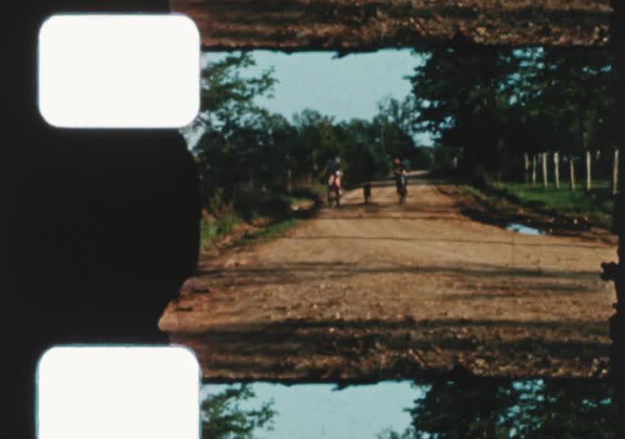Vintage 8mm film captures two happy children and their dog riding bicycles down a rural dirt road in the summer