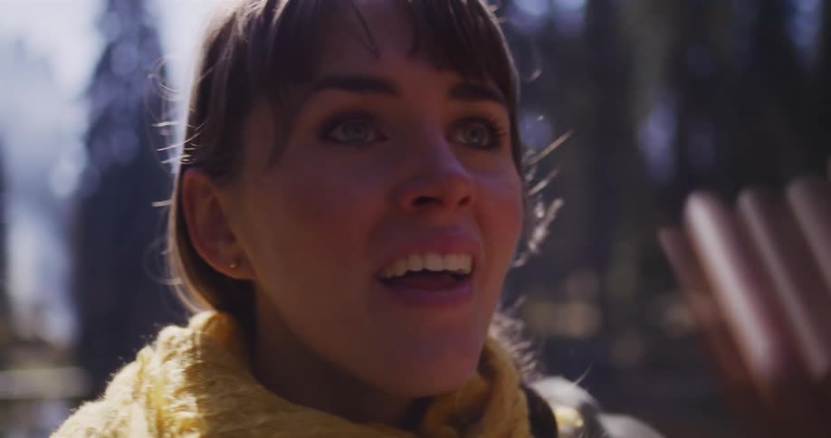 A woman wearing a yellow scarf looks up in awe and wonder while exploring a sunlit forest in slow motion
