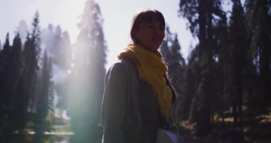 A woman with a yellow scarf takes a picture with an instant camera while standing in a sunlit forest