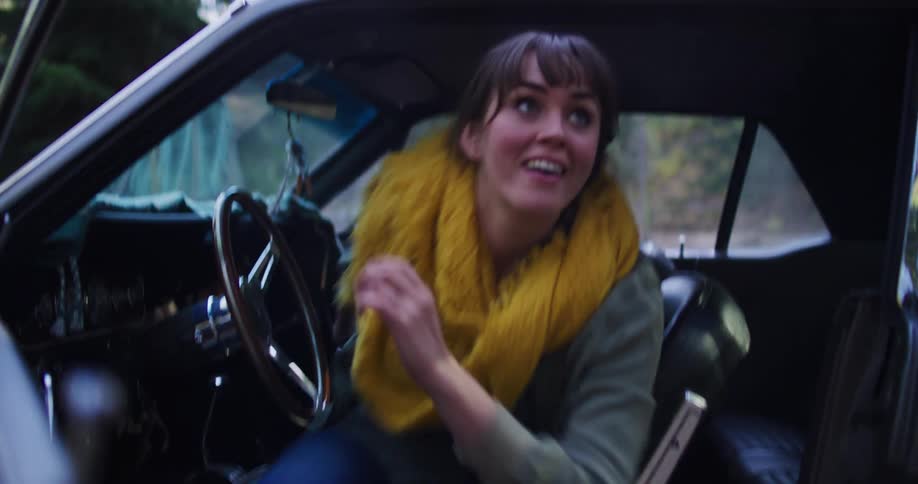 An excited young woman ties her boots before getting out of her vintage car to explore the forest