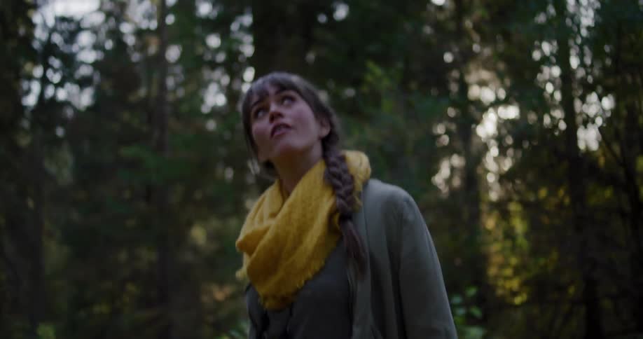 Awe-struck young woman with a yellow scarf gazes up at the sunlit canopy of a tranquil forest