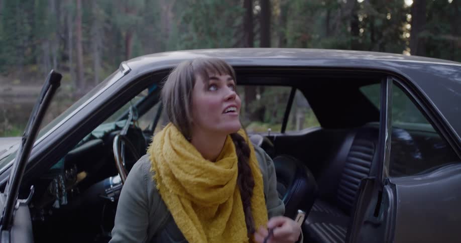 A young woman ties her boots and grabs her vintage camera, getting out of her classic car to explore the forest