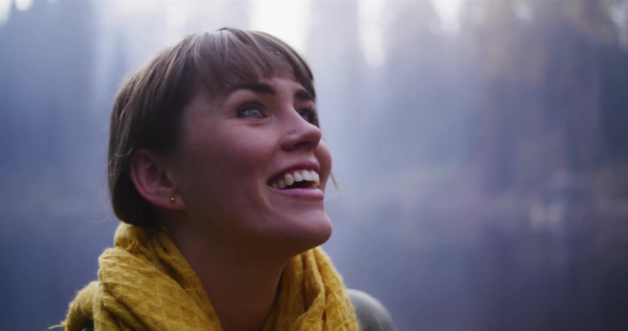Cinemagraph of a joyful young woman in a yellow scarf looking up in wonder at the light filtering through the misty air