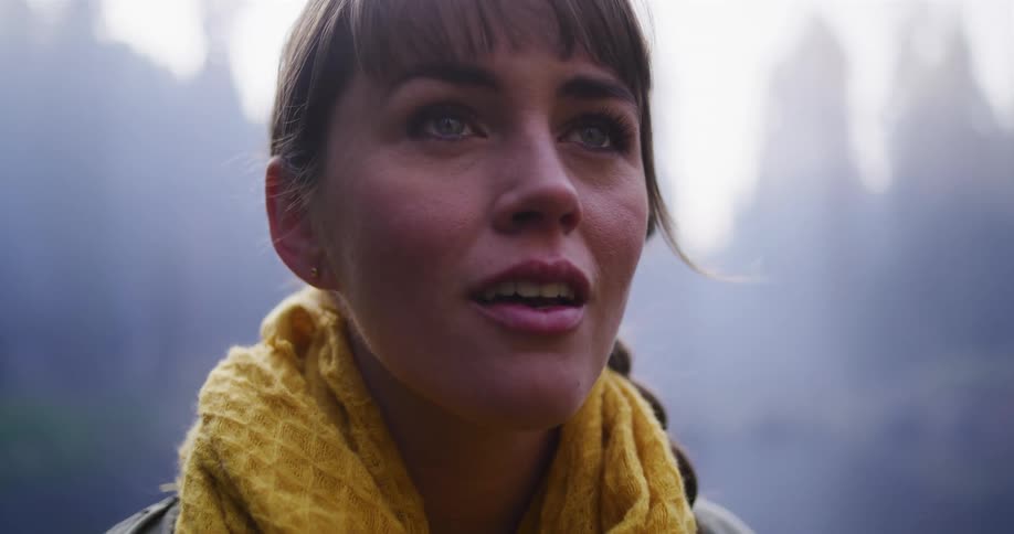 Close-up slow motion shot of a woman looking up in awe and wonder in a misty forest