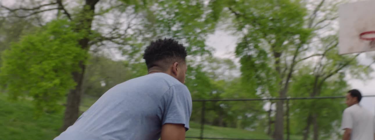 In slow motion, a focused young man shoots a basketball on an outdoor court, but misses the shot as it bounces off the rim