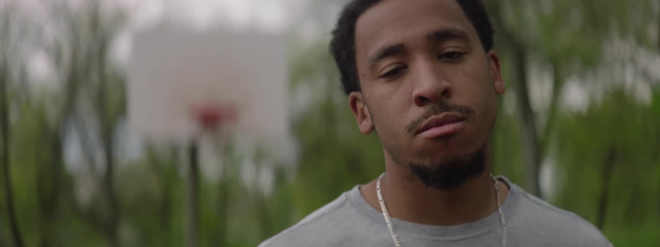 A rack focus shot moves from a basketball hoop to a close-up of a serious young man on an outdoor court