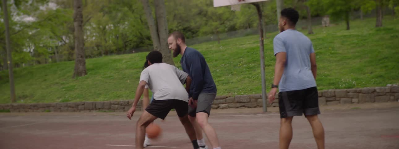 A group of diverse friends play basketball together on an outdoor court, culminating in a successful shot in slow motion