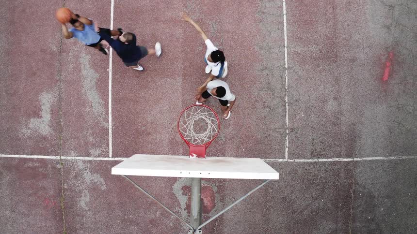Top-down aerial view of a diverse group of friends playing a slow-motion game of basketball on an outdoor court