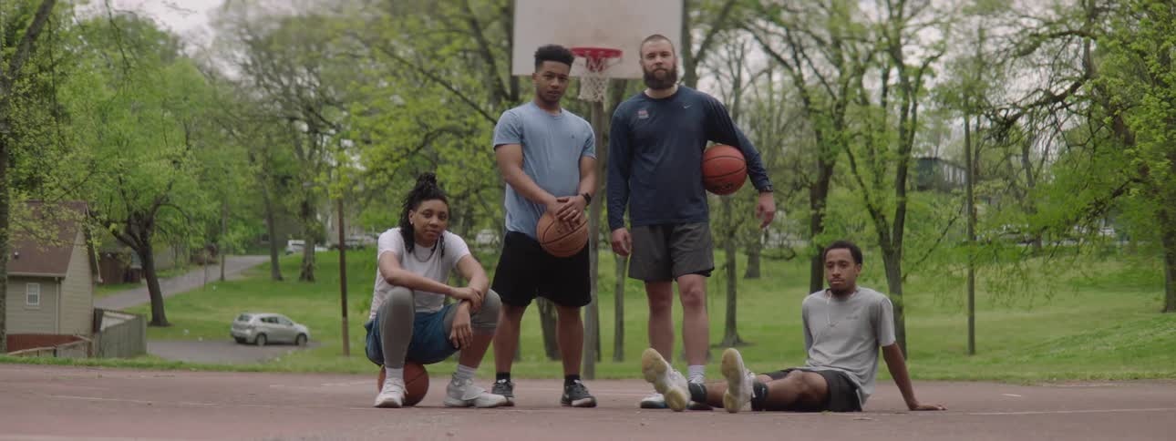 A group of four diverse friends pose together on an outdoor basketball court in a park