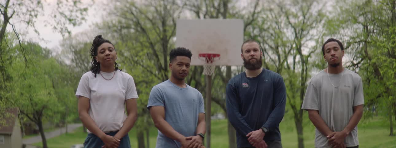 A diverse group of four basketball players pose for a team portrait on an outdoor court