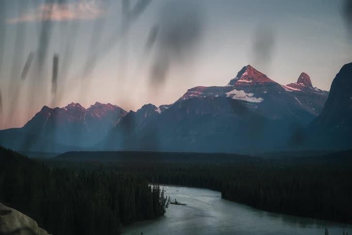 Time-lapse of a vibrant sunset fading to twilight over majestic snow-capped mountains, a winding river, and a vast evergreen forest